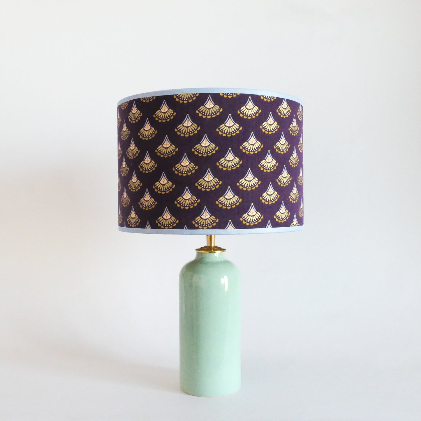 Ceramic table lamp with a mint green base and a purple lampshade featuring gold patterns on a white background