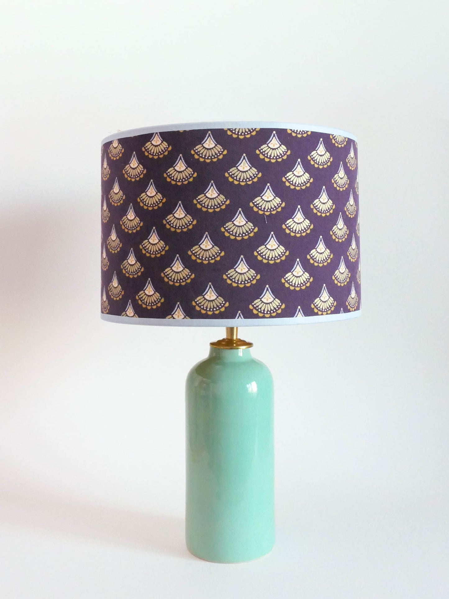 Ceramic table lamp with a mint green base and a purple lampshade featuring gold patterns on a white background