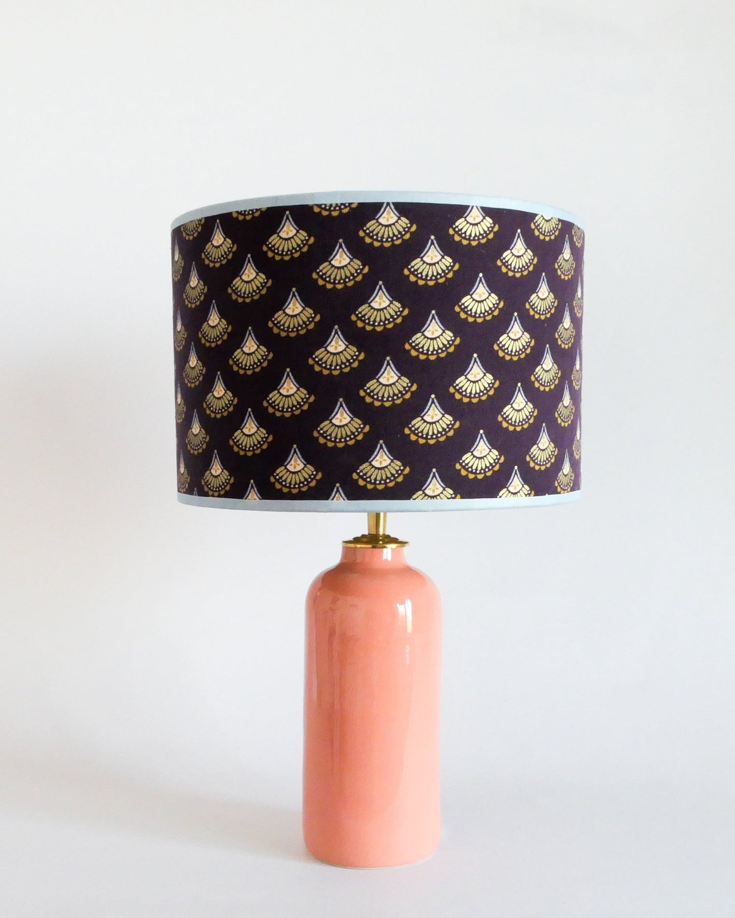 Ceramic table lamp with a pastel peach base and a purple lampshade featuring gold patterns on a white background