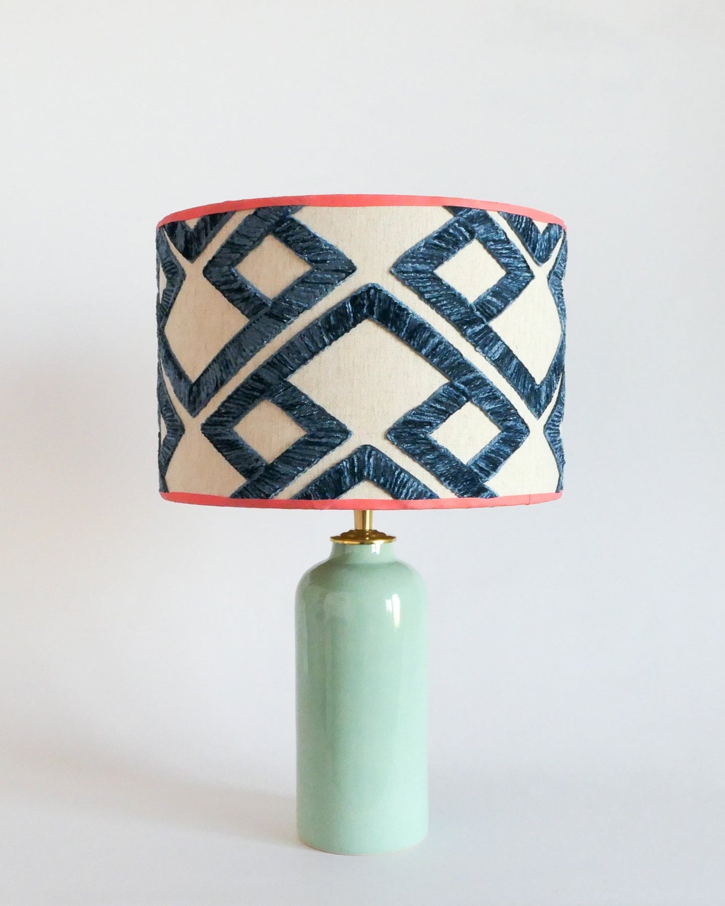 Ceramic table lamp with a mint green base and a geometric patterned shade on a white background