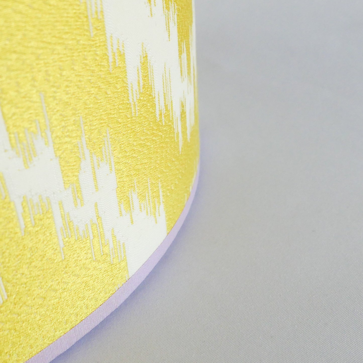Close up of a yellow and white patterned lampshade with a lila rim