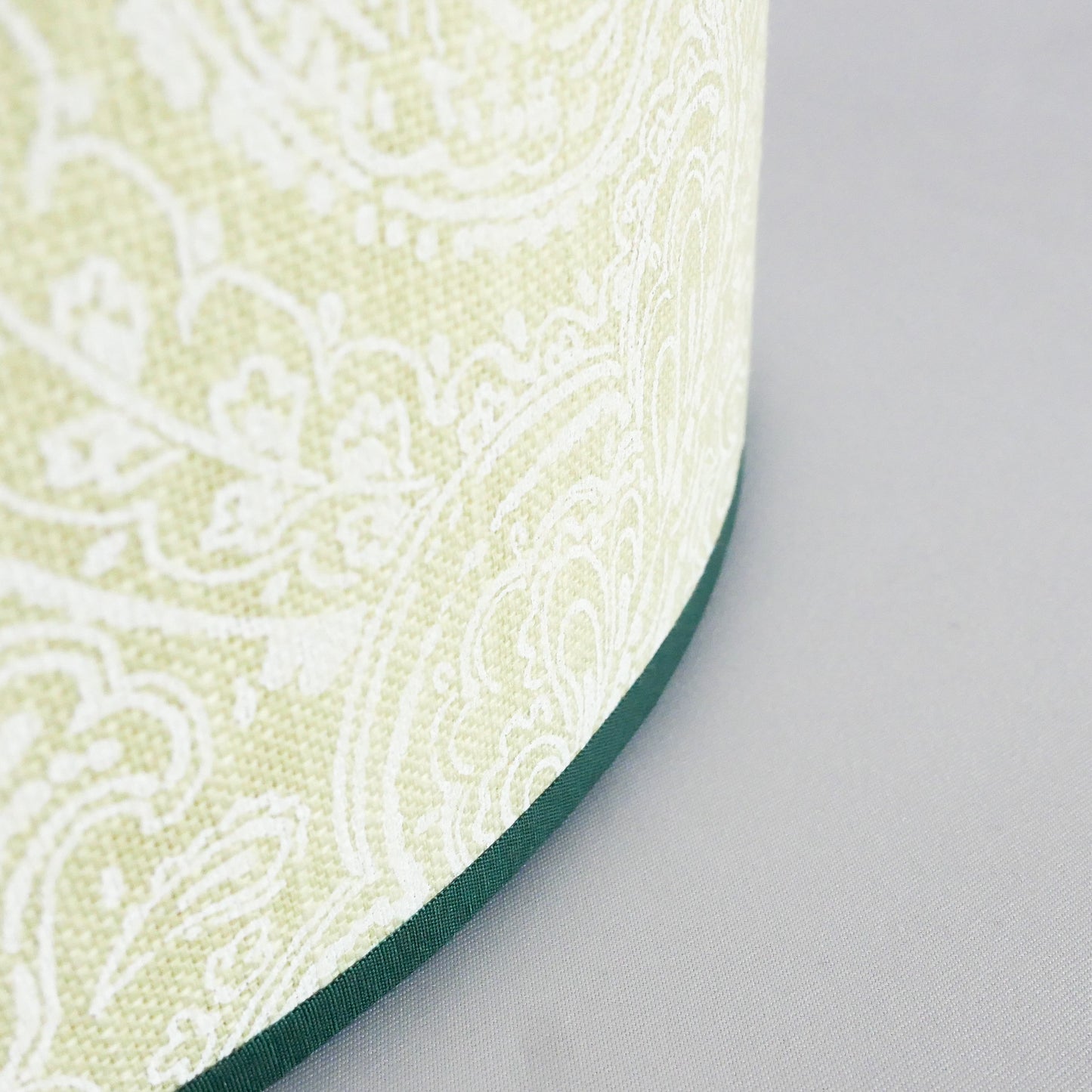 Close up of a lampshade with a light green pattern and a dark green rim