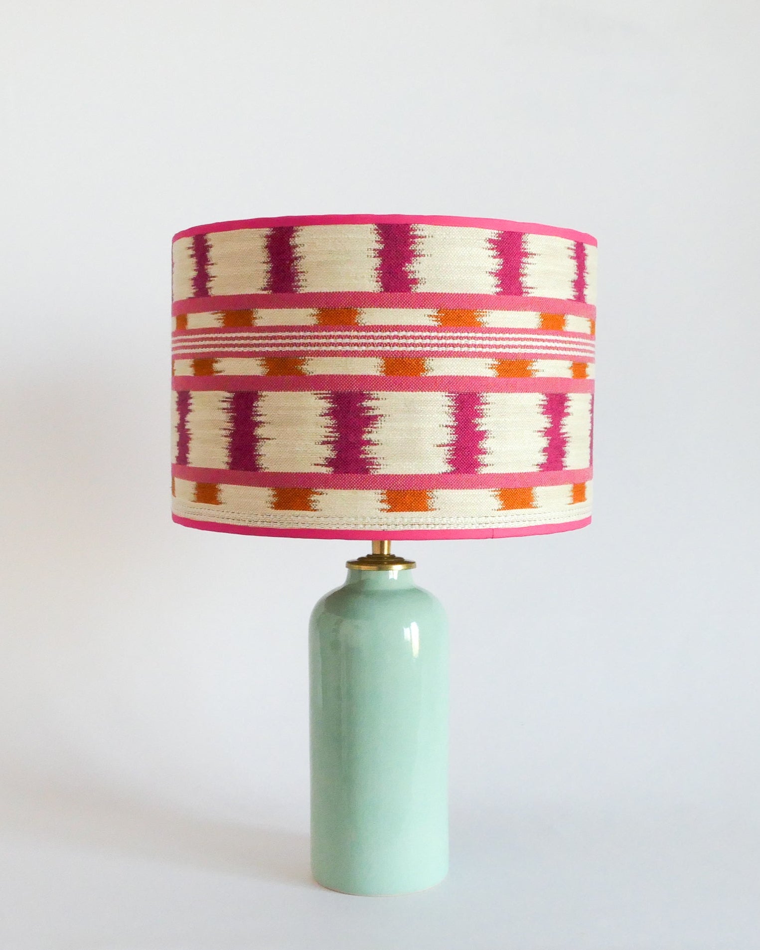 Ceramic table lamp with a colorful striped shade and a mint green base on a white background