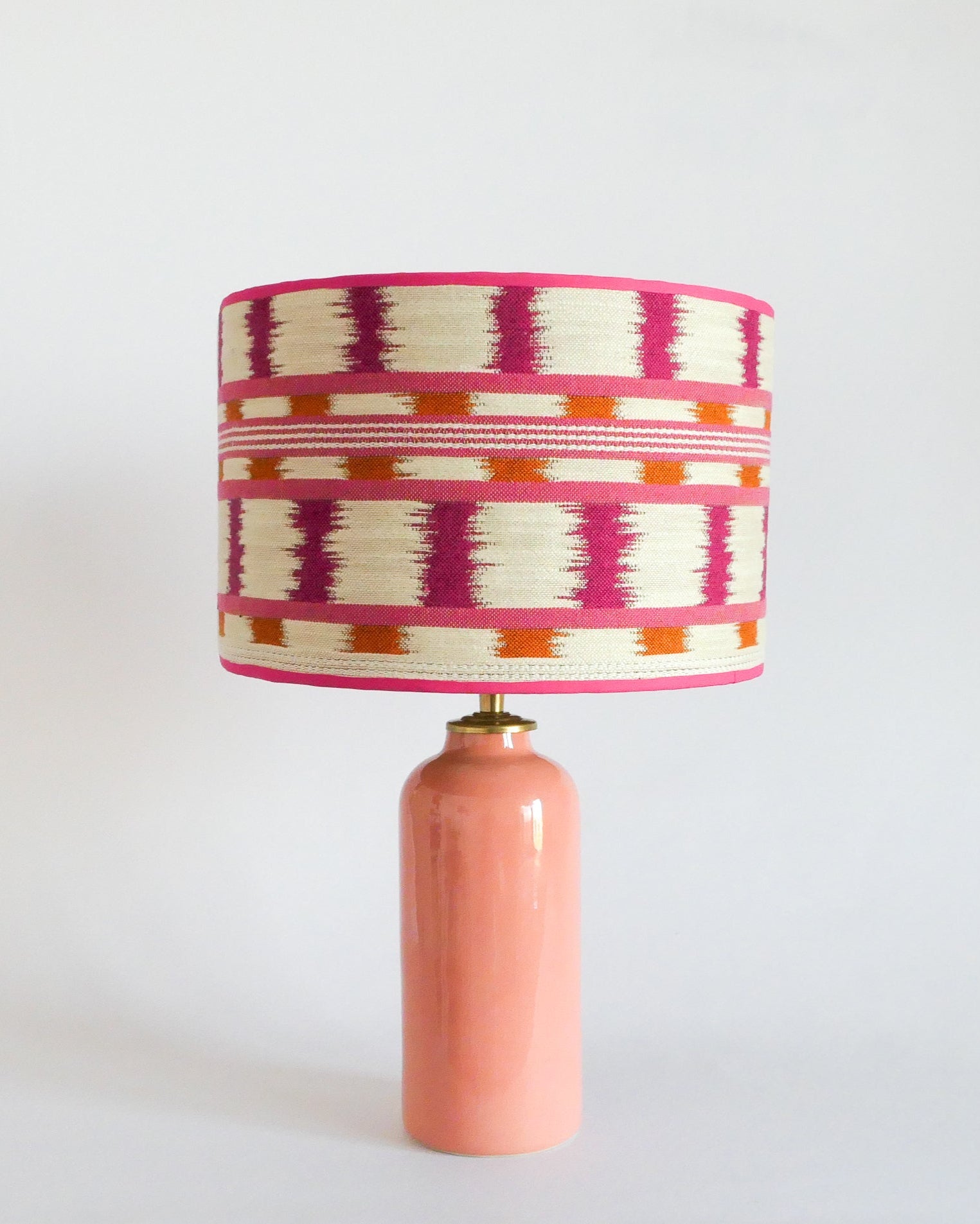 Ceramic table lamp with a colorful striped shade and a pastel peach base on a white background