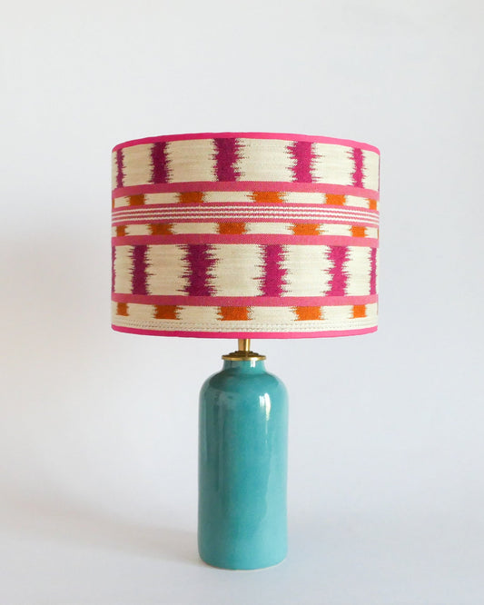 Ceramic table lamp with a colorful striped shade and a turquoise blue base on a white background
