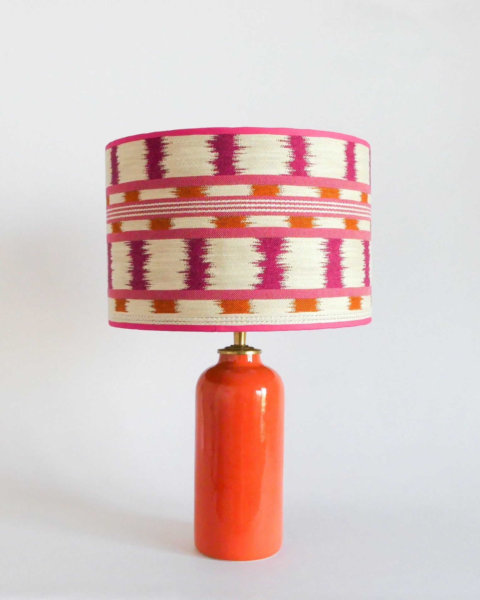 Ceramic table lamp with a colorful striped shade and an orange base on a white background