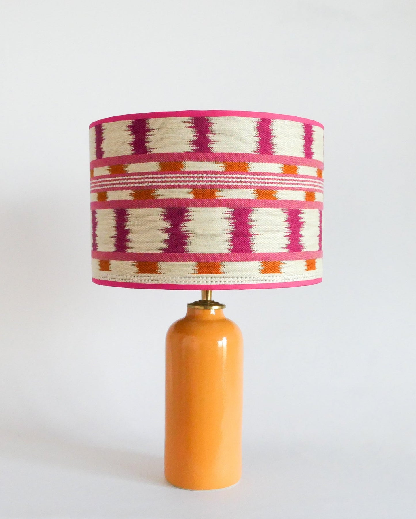 Ceramic table lamp with a colorful striped shade and a warm yellow base on a white background
