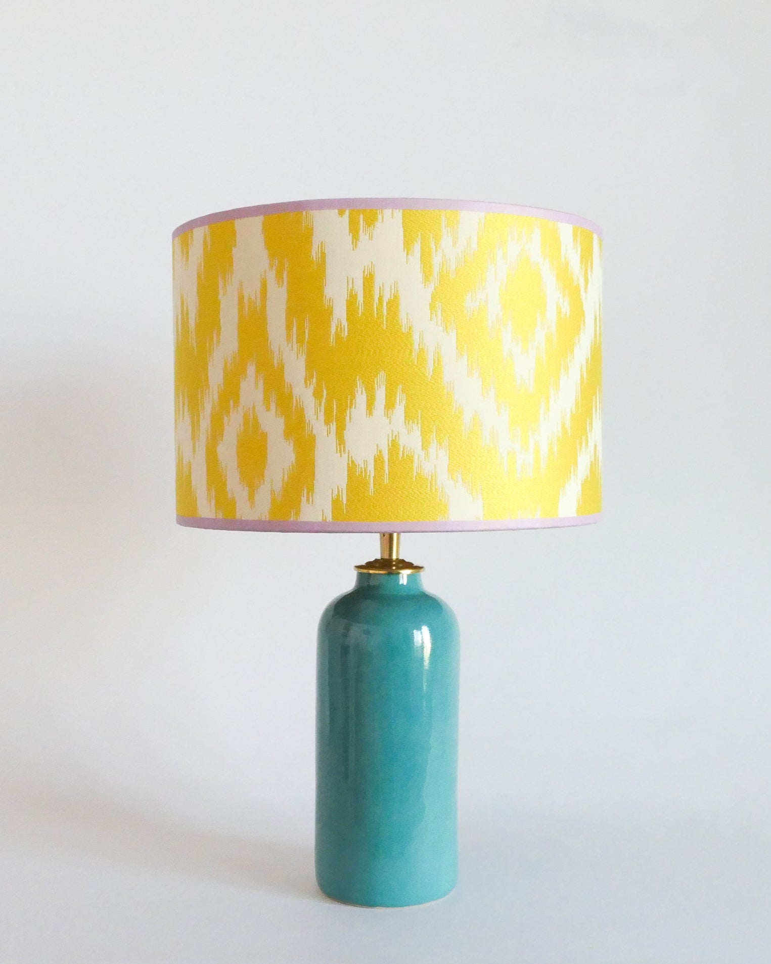 Ceramic table lamp with a yellow and white patterned shade on a turquoise blue base against a white background