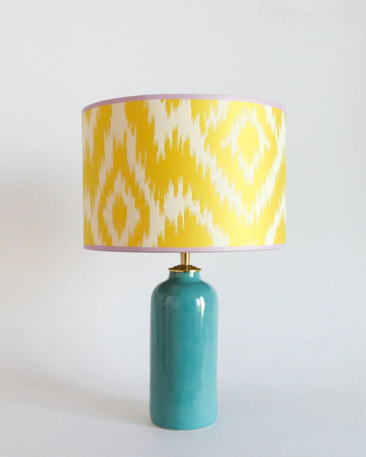 Ceramic table lamp with a yellow and white patterned shade on a turquoise blue base against a white background