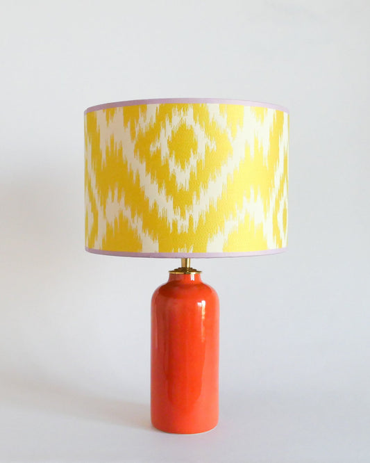 Ceramic table lamp with a yellow and white patterned shade on an orange base against a white background