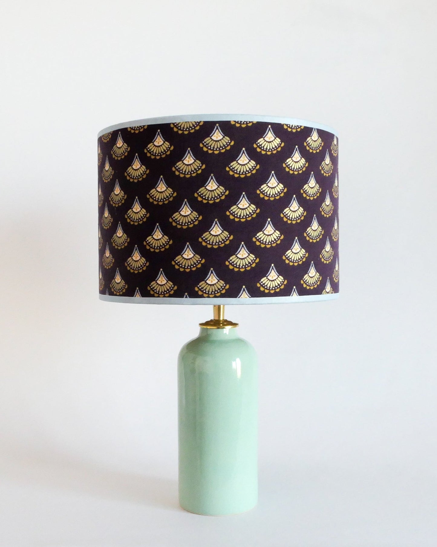 Ceramic table lamp with a mint green base and a purple lampshade featuring gold patterns on a white background