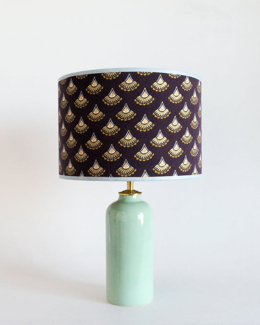 Ceramic table lamp with a mint green base and a purple lampshade featuring gold patterns on a white background