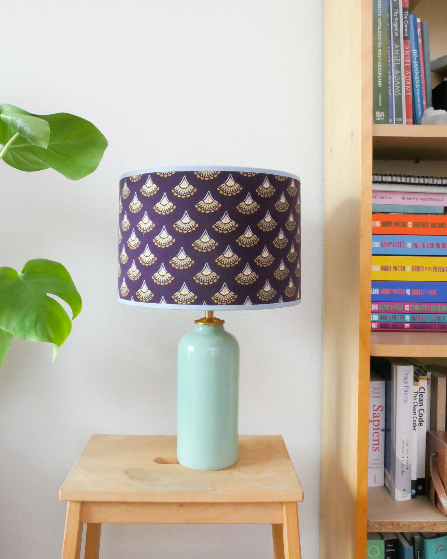 Tafellamp met een paarse lampenkap en een mint groene lampenvoet op een krukje naast een boekenkast.