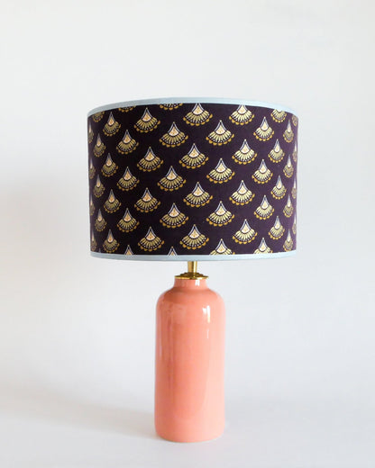 Ceramic table lamp with a pastel peach base and a purple lampshade featuring gold patterns on a white background