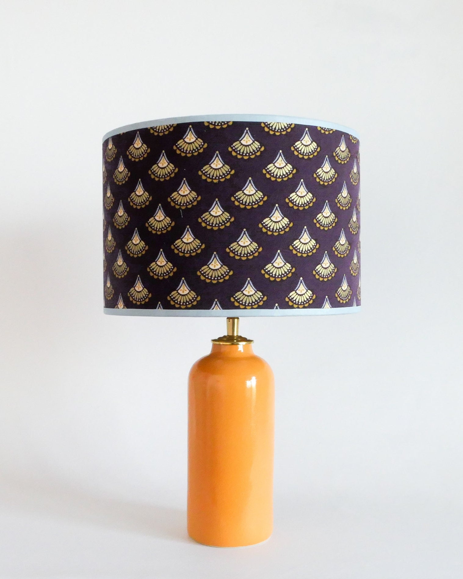 Ceramic table lamp with a purple shade featuring gold patterns on a warm yellow lamp base.