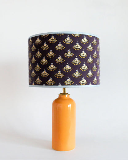 Ceramic table lamp with a purple shade featuring gold patterns on a warm yellow lamp base.
