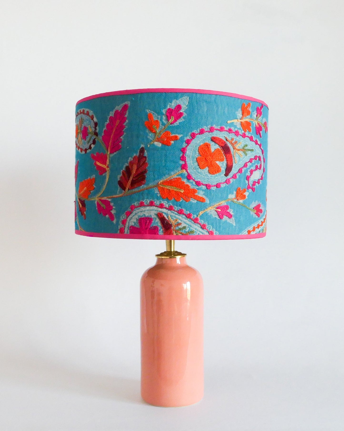 Ceramic table lamp with a blue embroidered shade with floral patterns on a pastel peach lamp base