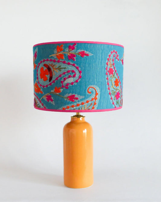 Ceramic table lamp with a blue embroidered lampshade with floral patterns on a warm yellow lamp base.