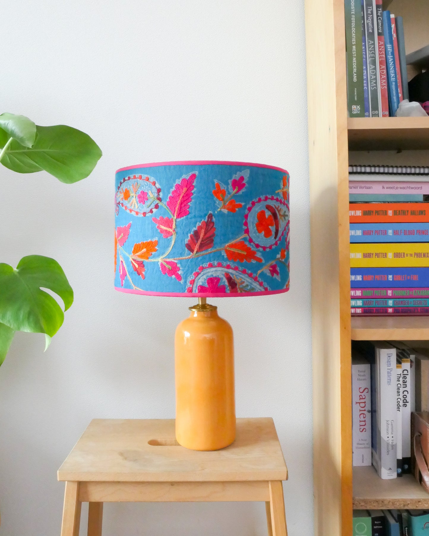 Tafellamp met een blauwe lampenkap en een gele lampenvoet op een krukje naast een boekenkast.