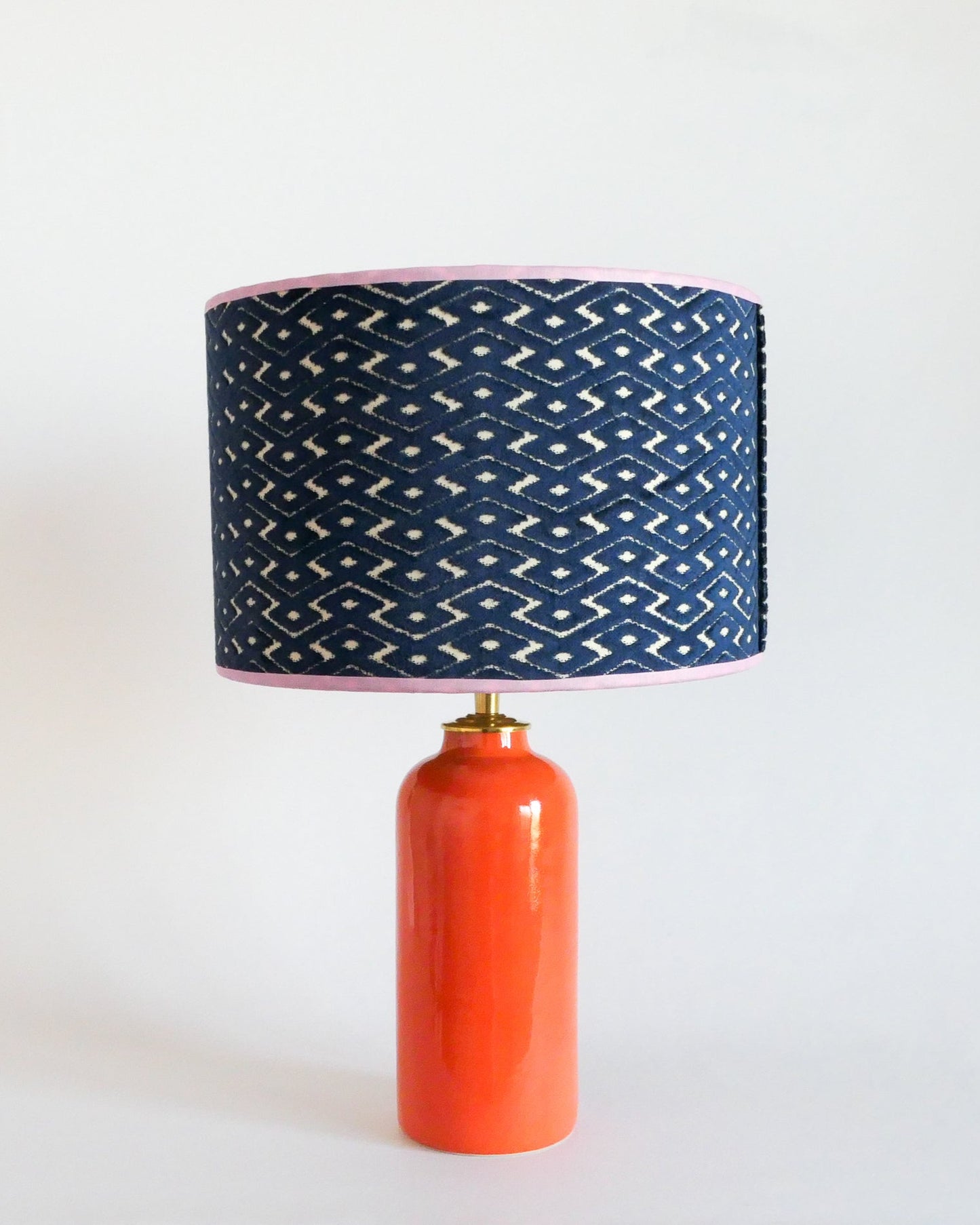 Ceramic table lamp with a blue patterned shade and an orange base on a white background