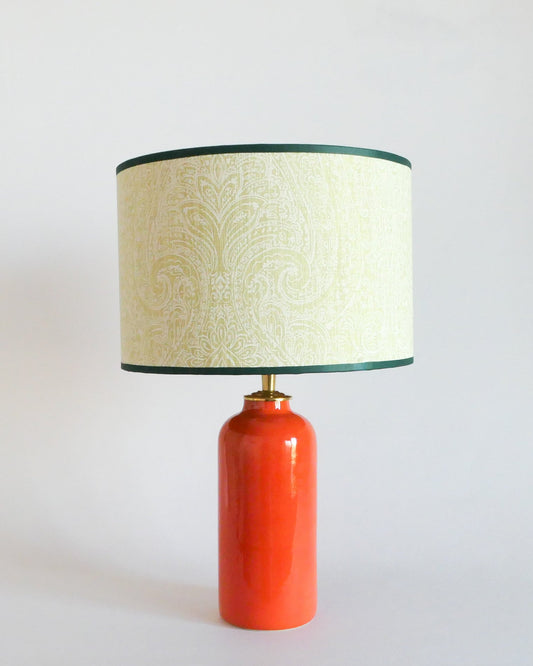 Ceramic table lamp with an orange base and a light green patterned shade on a white background