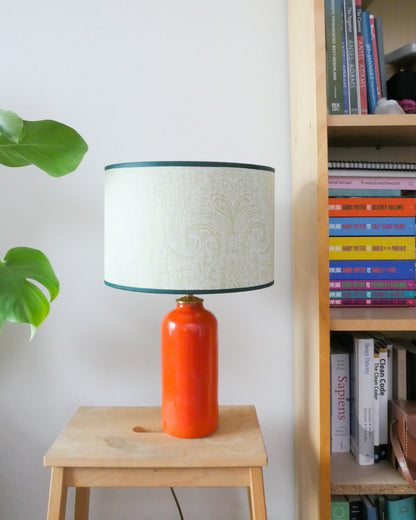 Tafellamp met een lichtgroene lampenkap en een knal oranje lampenvoet op een krukje naast een boekenkast.