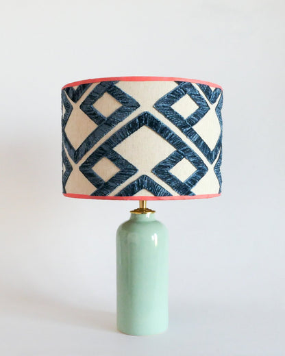 Ceramic table lamp with a mint green base and a geometric patterned shade on a white background