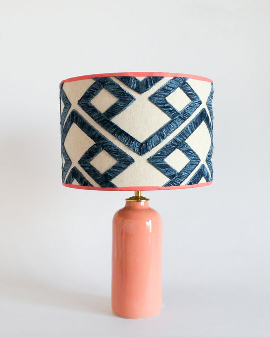 Ceramic table lamp with a pastel peach base and a geometric patterned shade on a white background