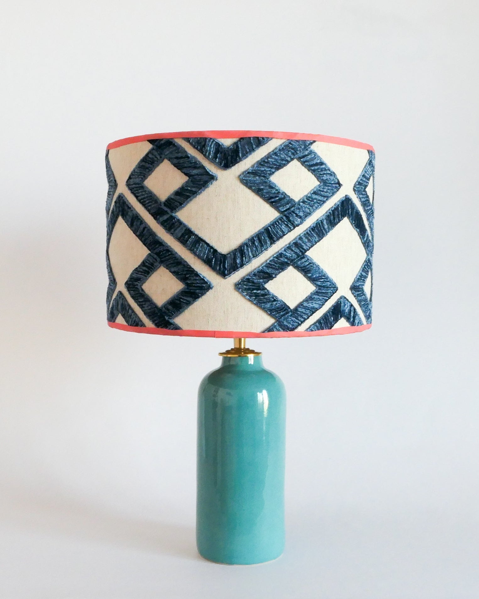 Ceramic table lamp with a turquoise blue base and a geometric patterned shade on a white background