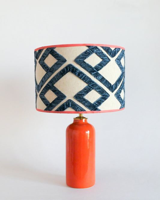 Ceramic table lamp with an orange base and a geometric patterned shade on a white background