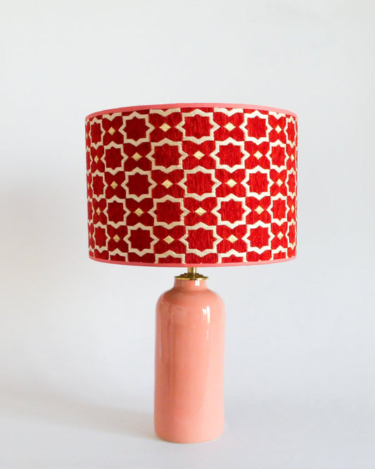 Ceramic table lamp with a red and white patterned shade on a pastel peach base against a white background