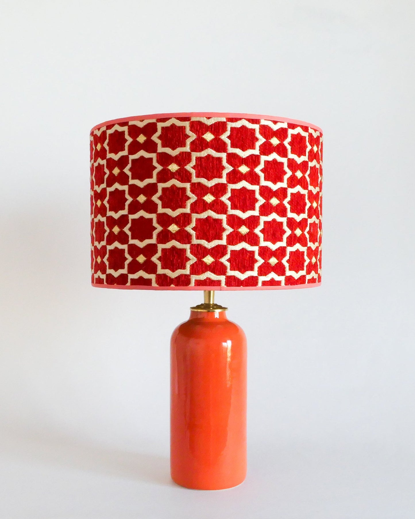 Ceramic table lamp with a red and white patterned shade on an orange base against a white background
