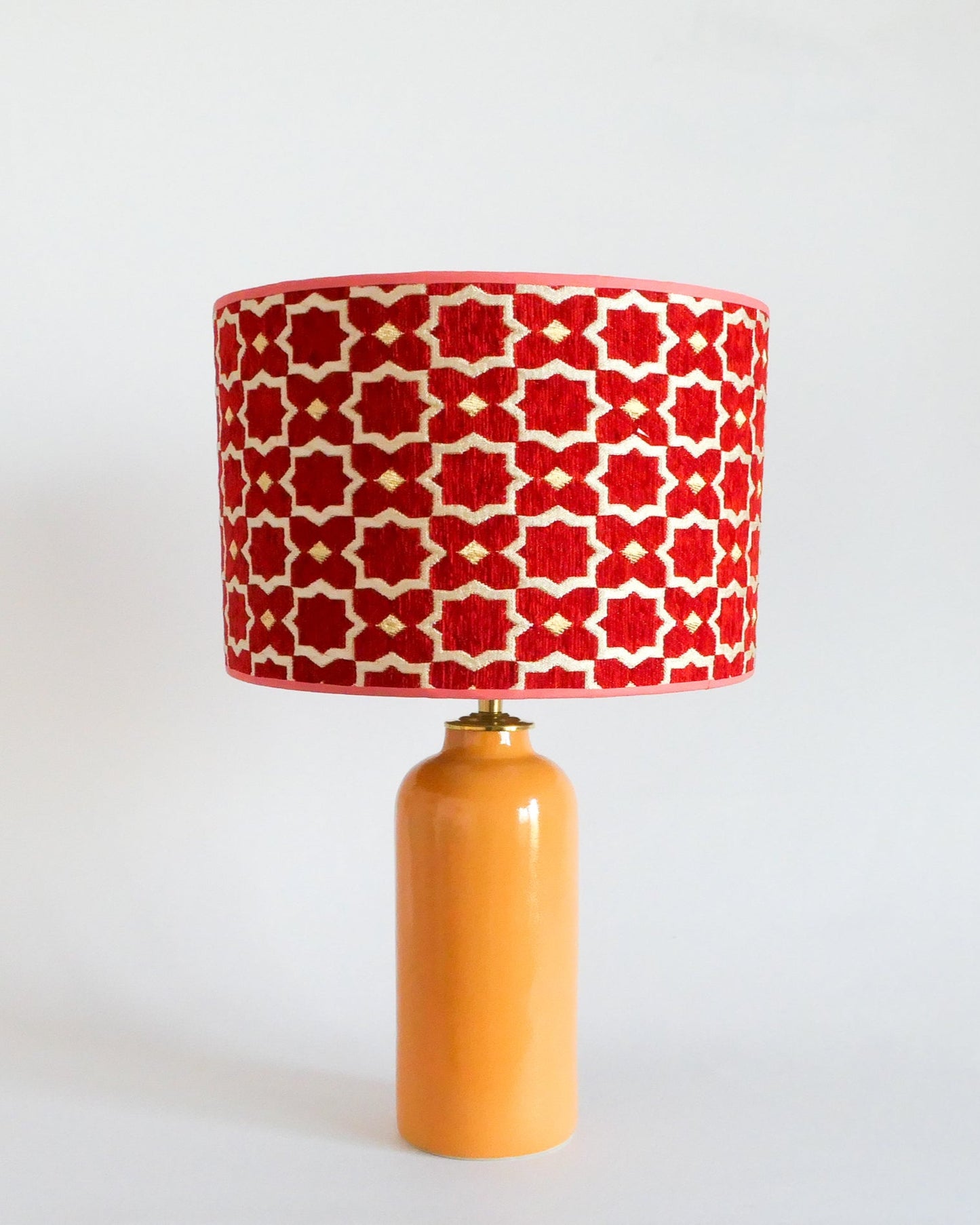 Ceramic table lamp with a red and white patterned shade on a warm yellow base against a white background
