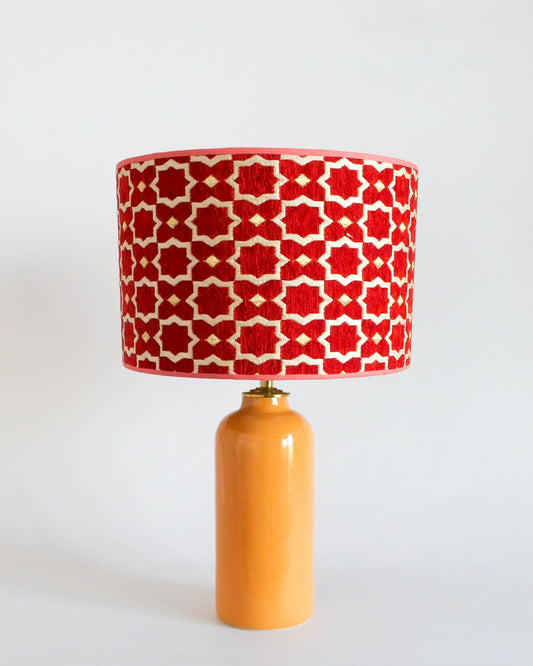 Ceramic table lamp with a red and white patterned shade on a warm yellow base against a white background