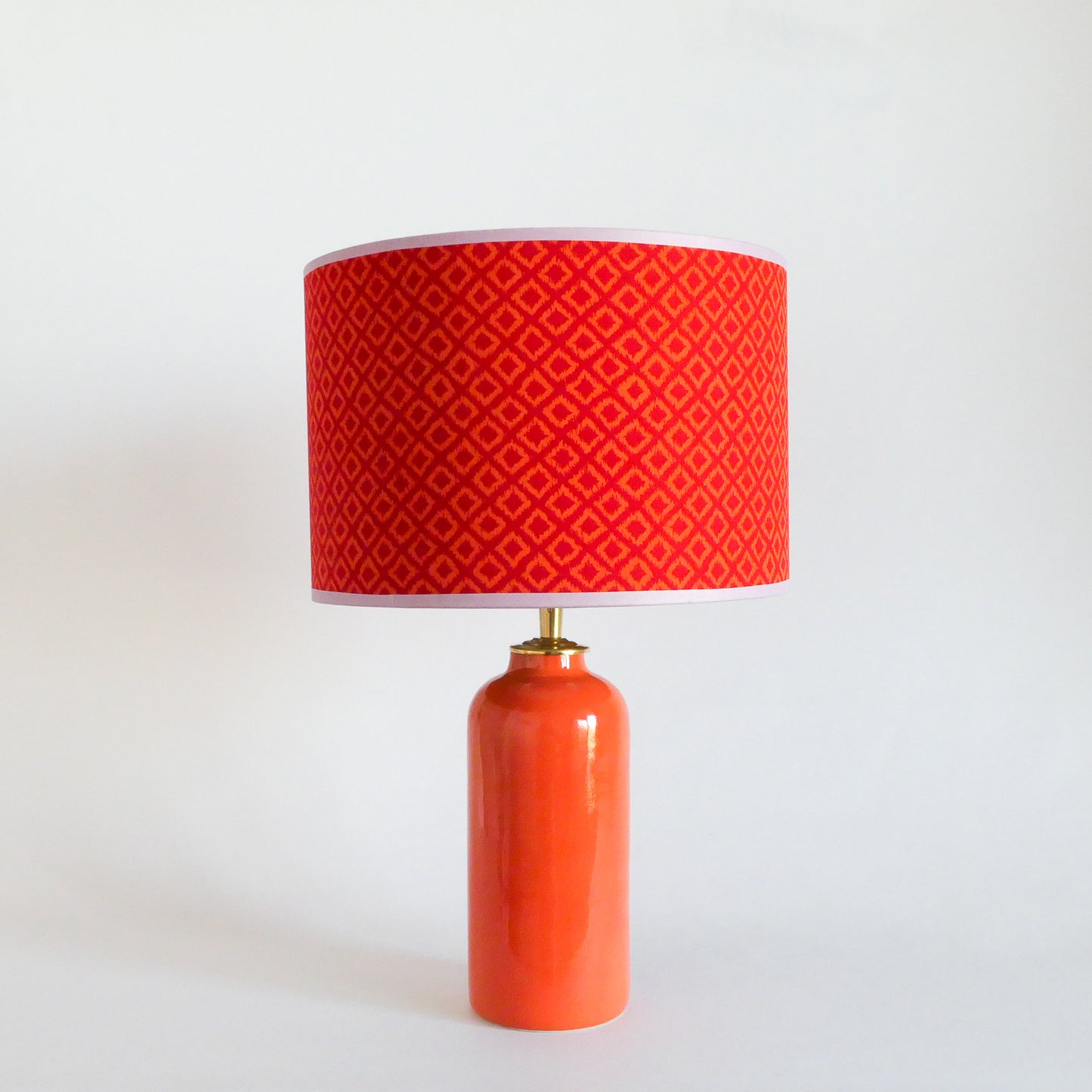 Orange ceramic table lamp with a red patterned shade on a white background