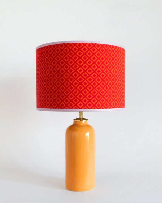 Ceramic table lamp with a red patterned shade and a warm yellow base on a white background