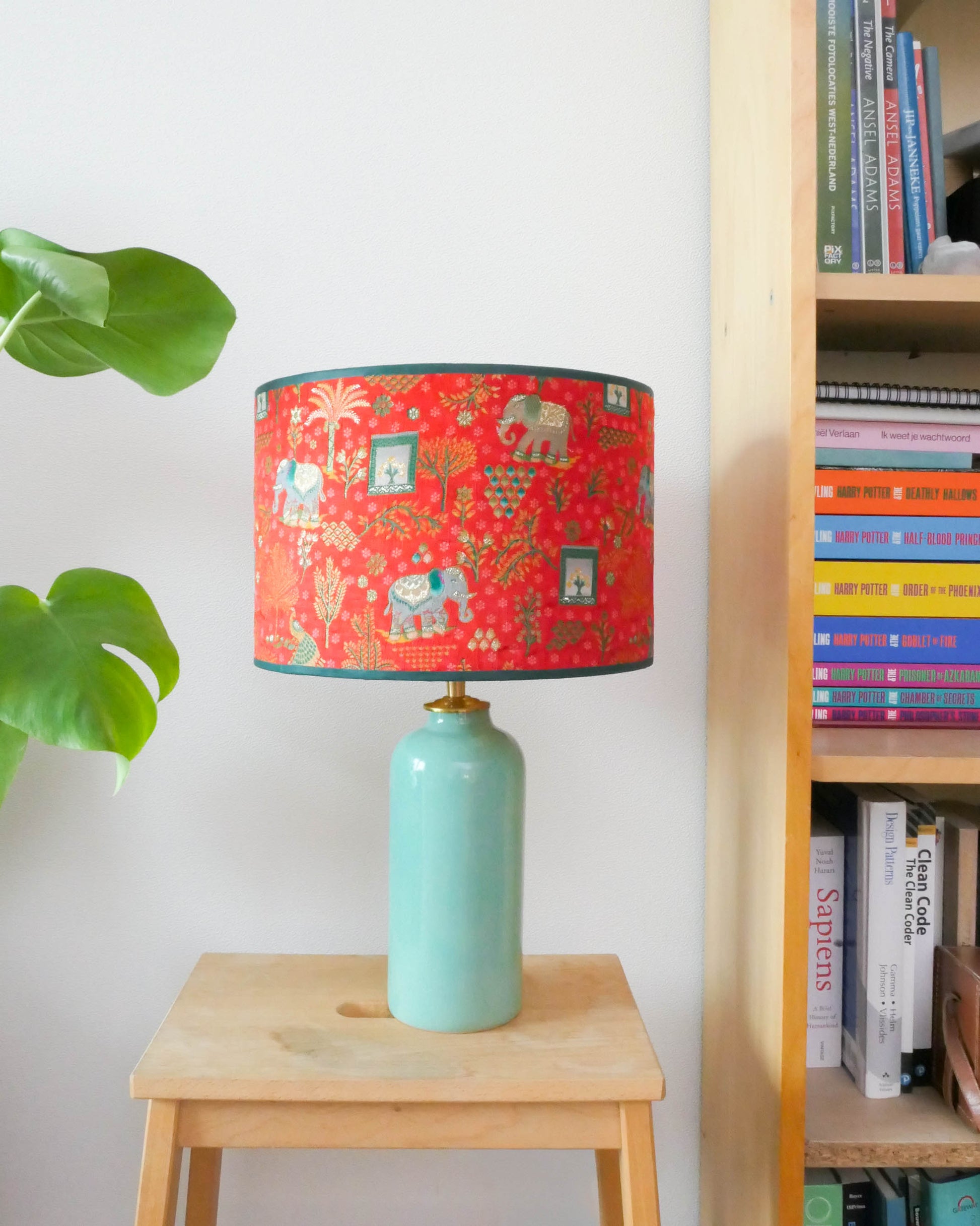 Tafellamp met een rode lampenkap en een licht groene lampenvoet op een krukje naast een boekenkast.