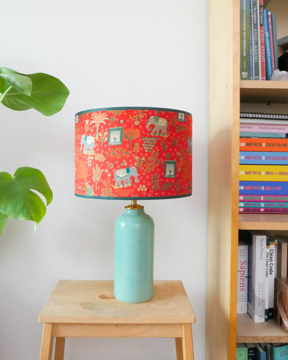 Tafellamp met een rode lampenkap en een licht groene lampenvoet op een krukje naast een boekenkast.