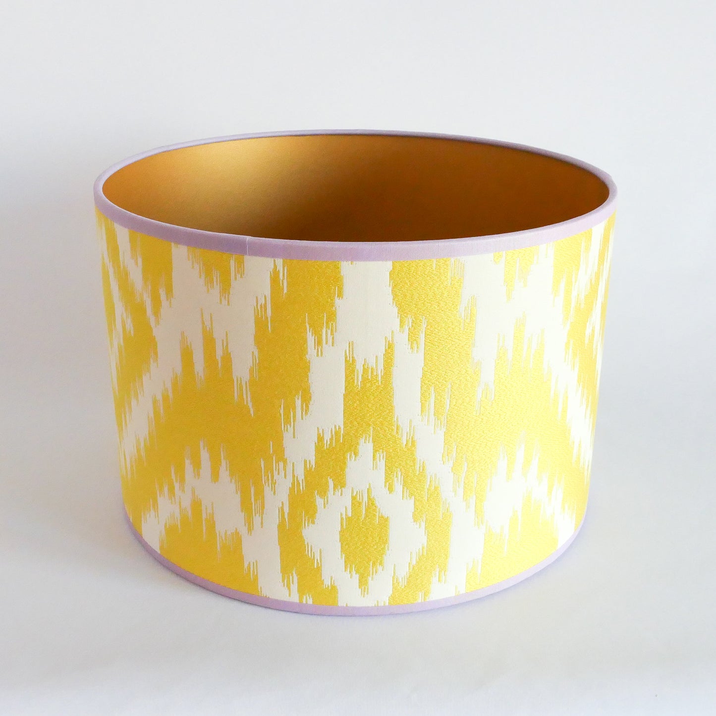 Top view of a yellow and white patterned lampshade with a gold interior and a lila rim