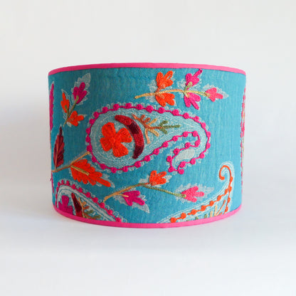 Front view of a blue embroidered lampshade with floral patterns and a pink rim.
