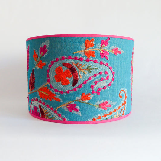Front view of a blue embroidered lampshade with floral patterns and a pink rim.
