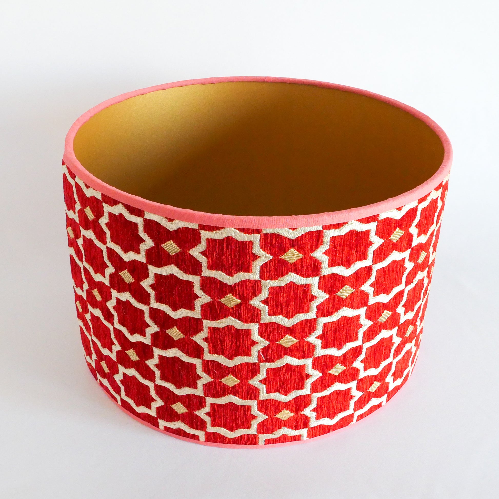 Top view of a red and white patterned lampshade with a gold interior on a white background