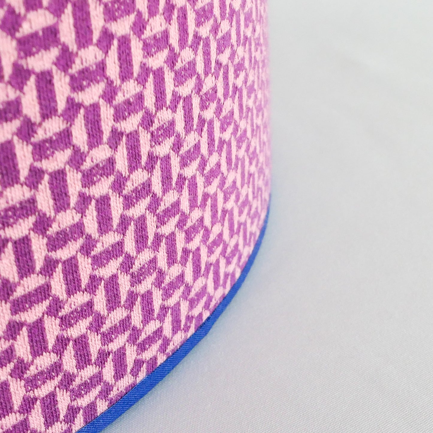 Close up of a lampshade with a pink geometric pattern and blue rim on a white background