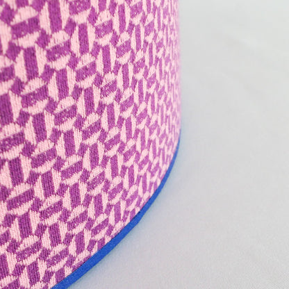 Close up of a lampshade with a pink geometric pattern and blue rim on a white background