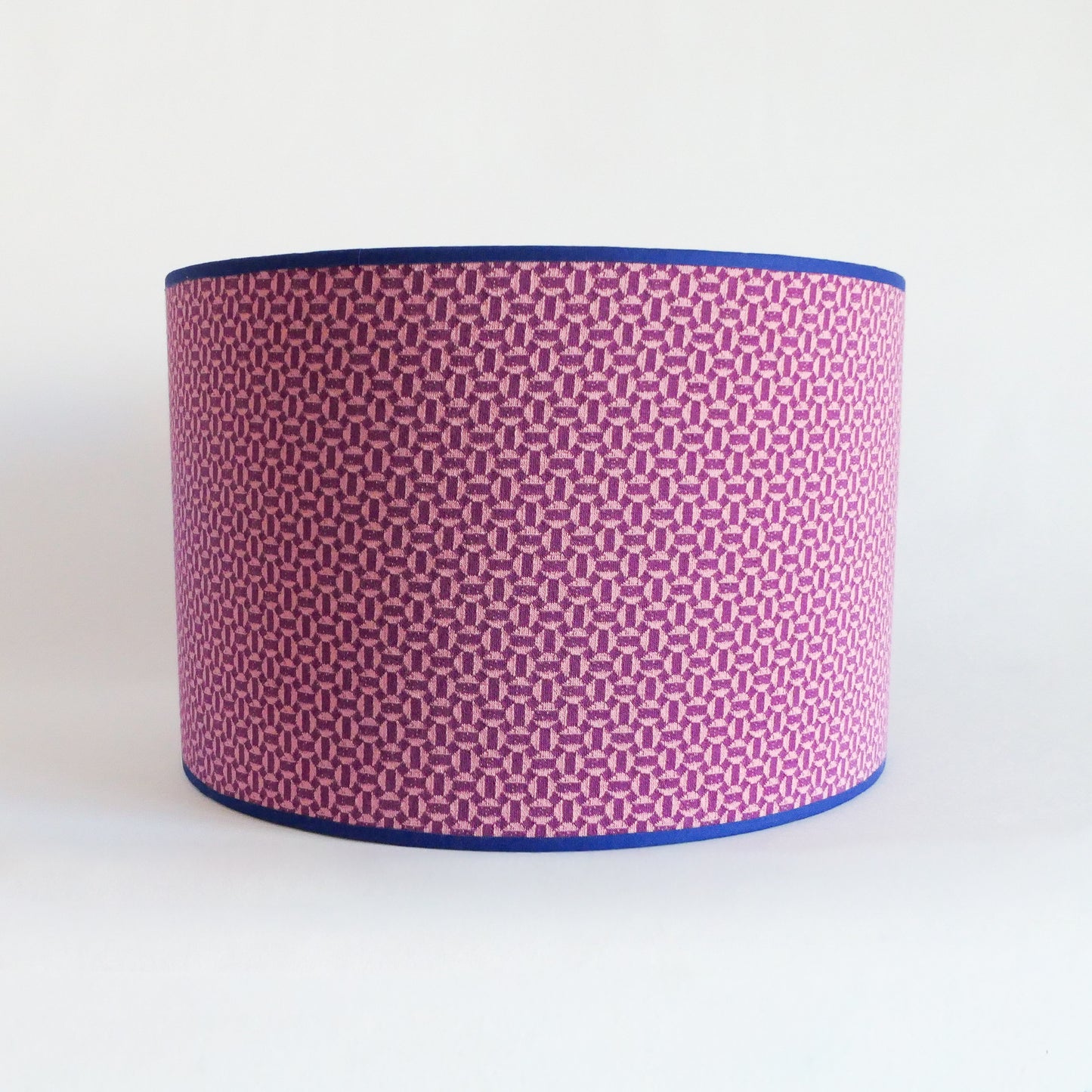 Front view of a lampshade with a pink geometric pattern and blue rim on a white background