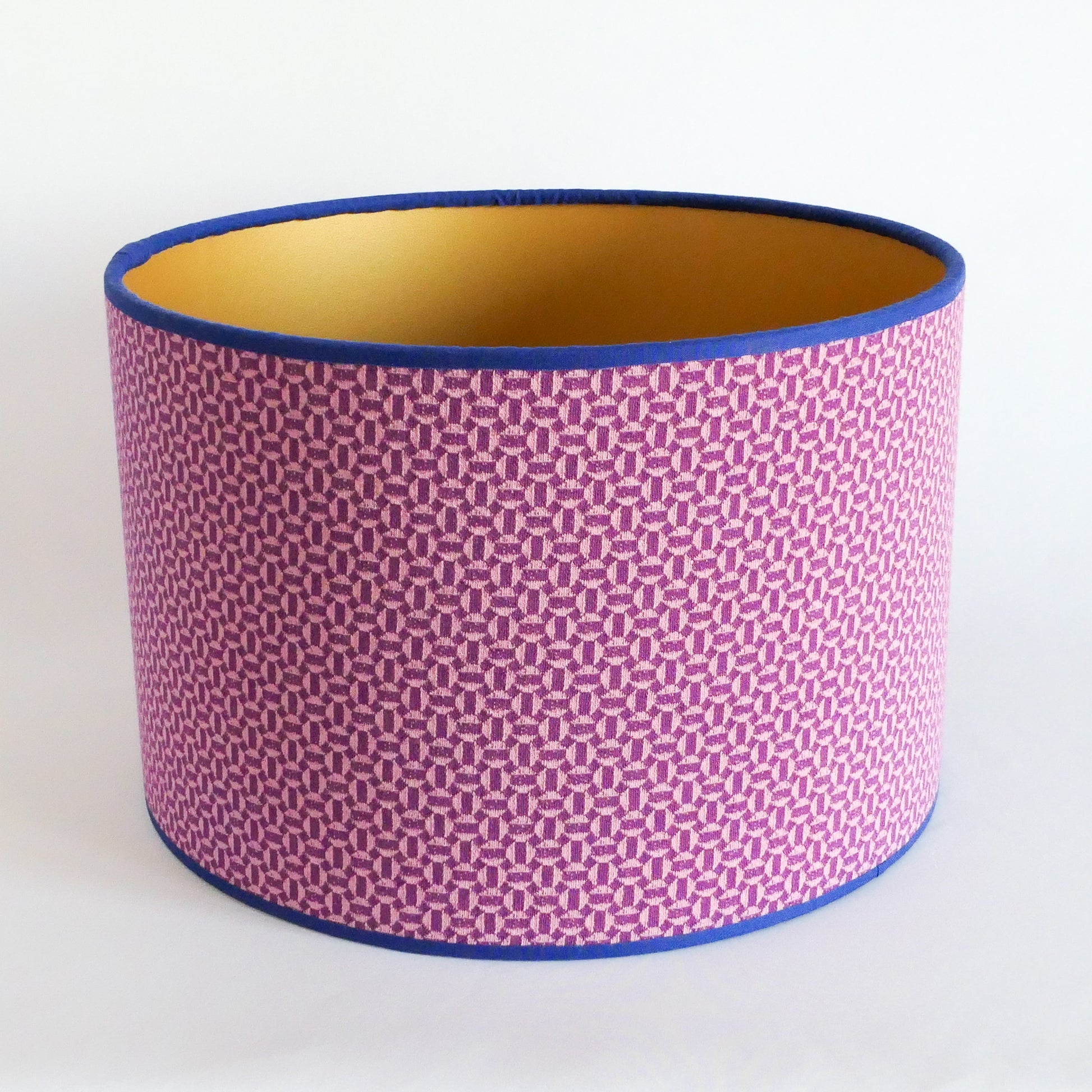 Top view of a lampshade with a pink geometric pattern and blue rim and a gold interior on a white background
