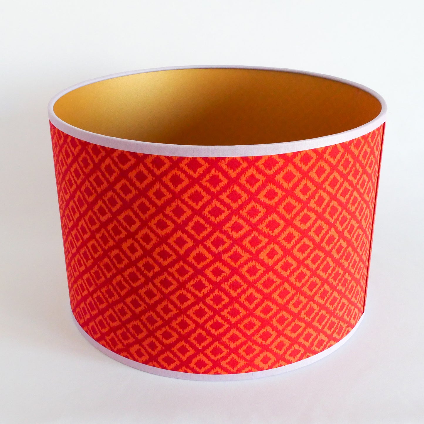 Top view of a red patterned lampshade with gold interior on a white background