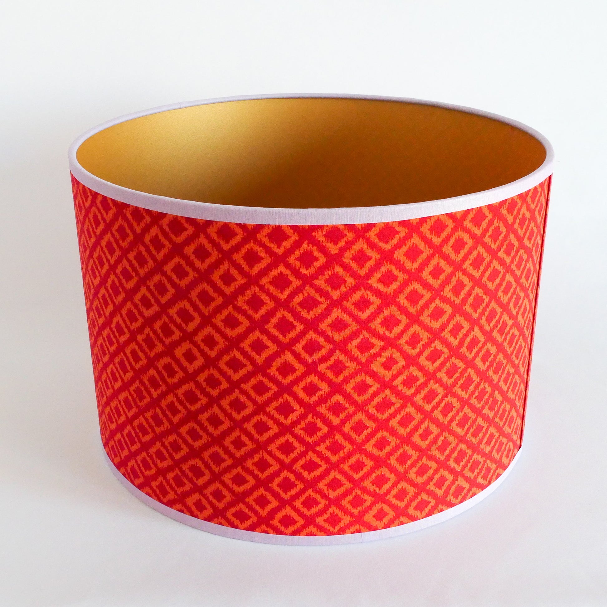 Top view of a red patterned lampshade with gold interior on a white background